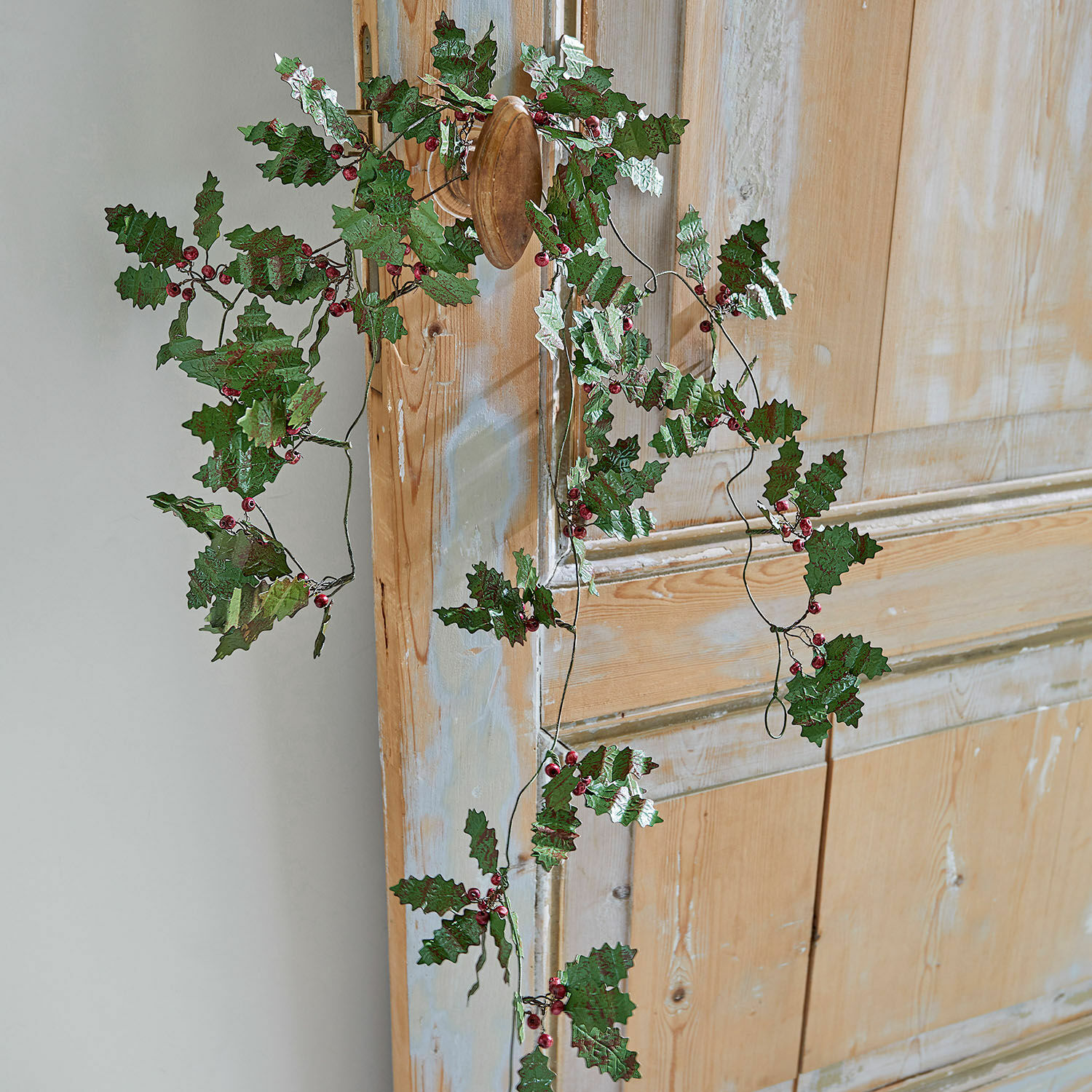 Decoratieve krans met groene bladeren en rode bessen aan houten deur, feestelijke kerstversiering