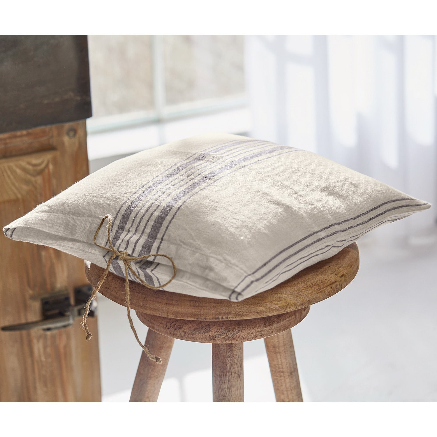 Decoratief linnen kussen in crème met grijze strepen op een houten kruk