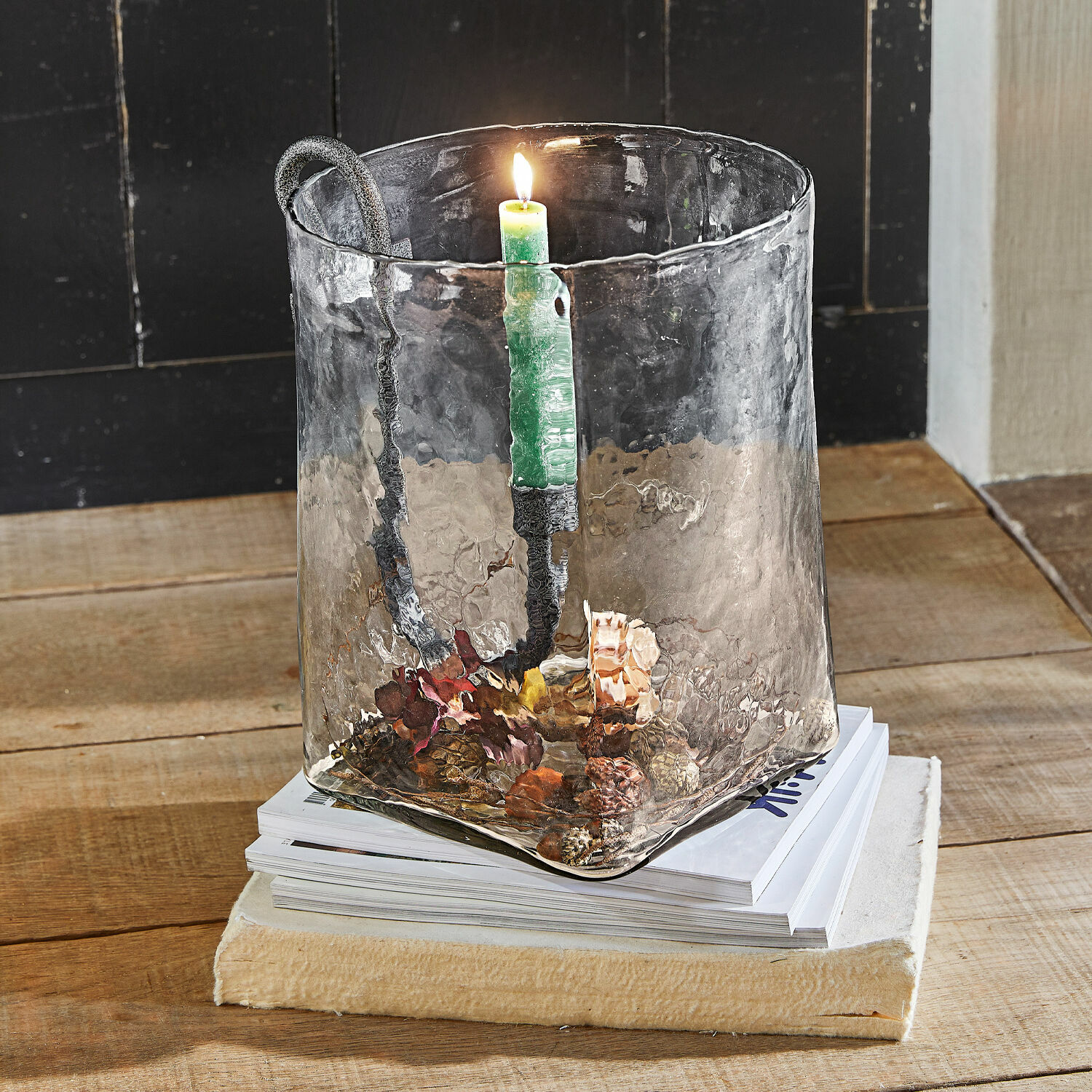 Glazen kandelaar met metalen handvat en groene kaars op houten tafel met dennenappeldecoratie