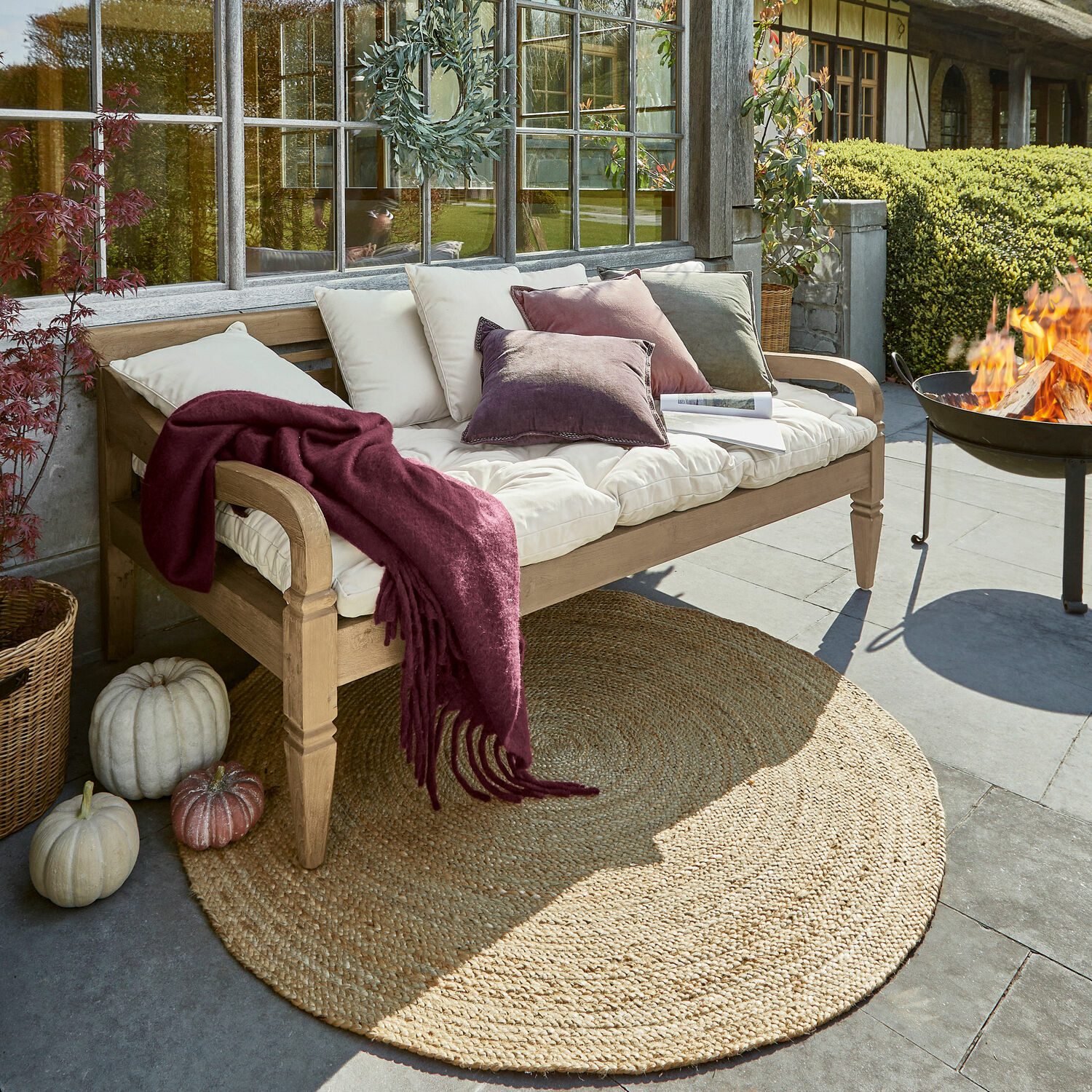 Bank Fairwood Houten tuinbank met crèmekleurige kussens en bordeauxrode deken op terras met jute vloerkleed