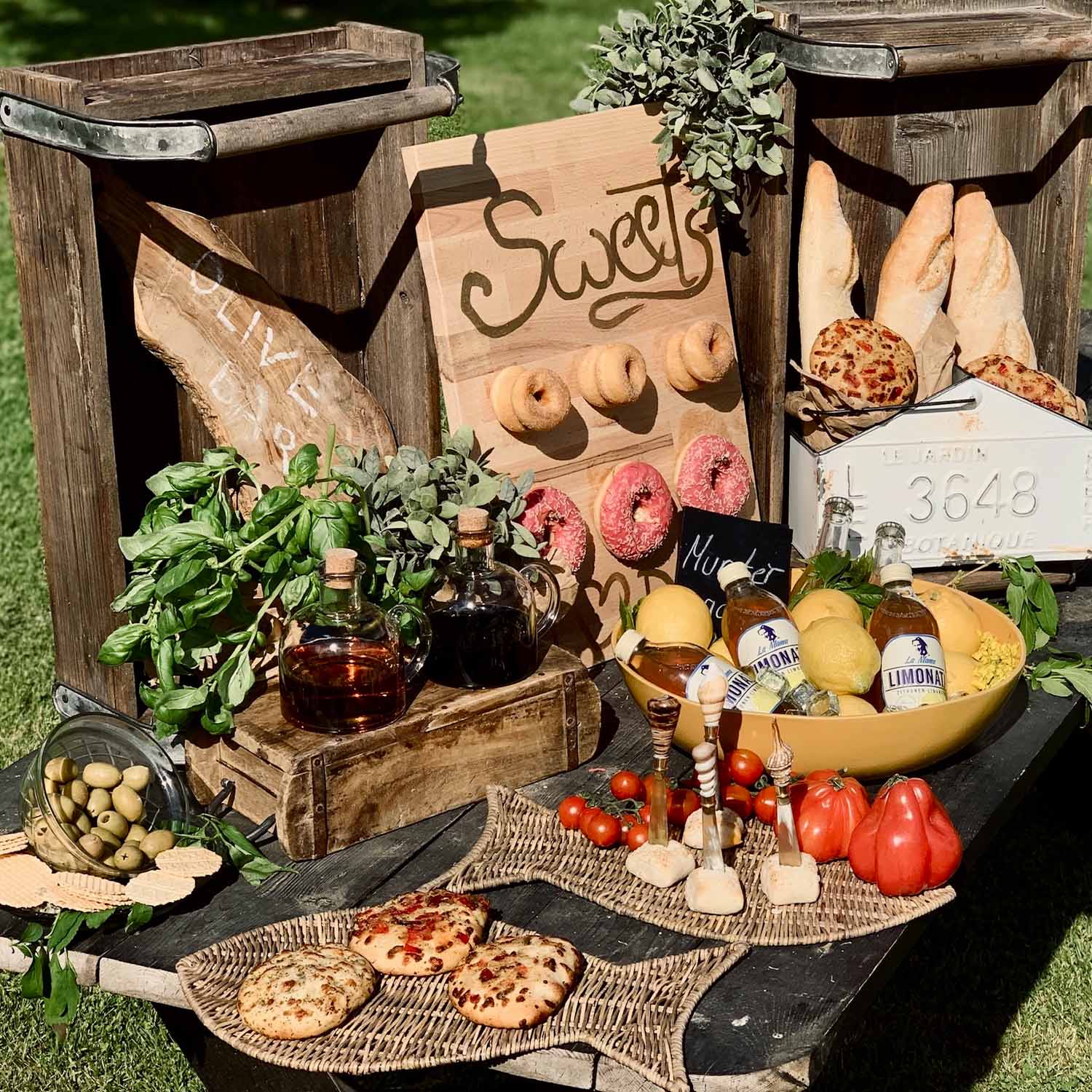 Rustieke tafel met houten kisten, brood, olijven, kruiden en limonade buiten in de zon