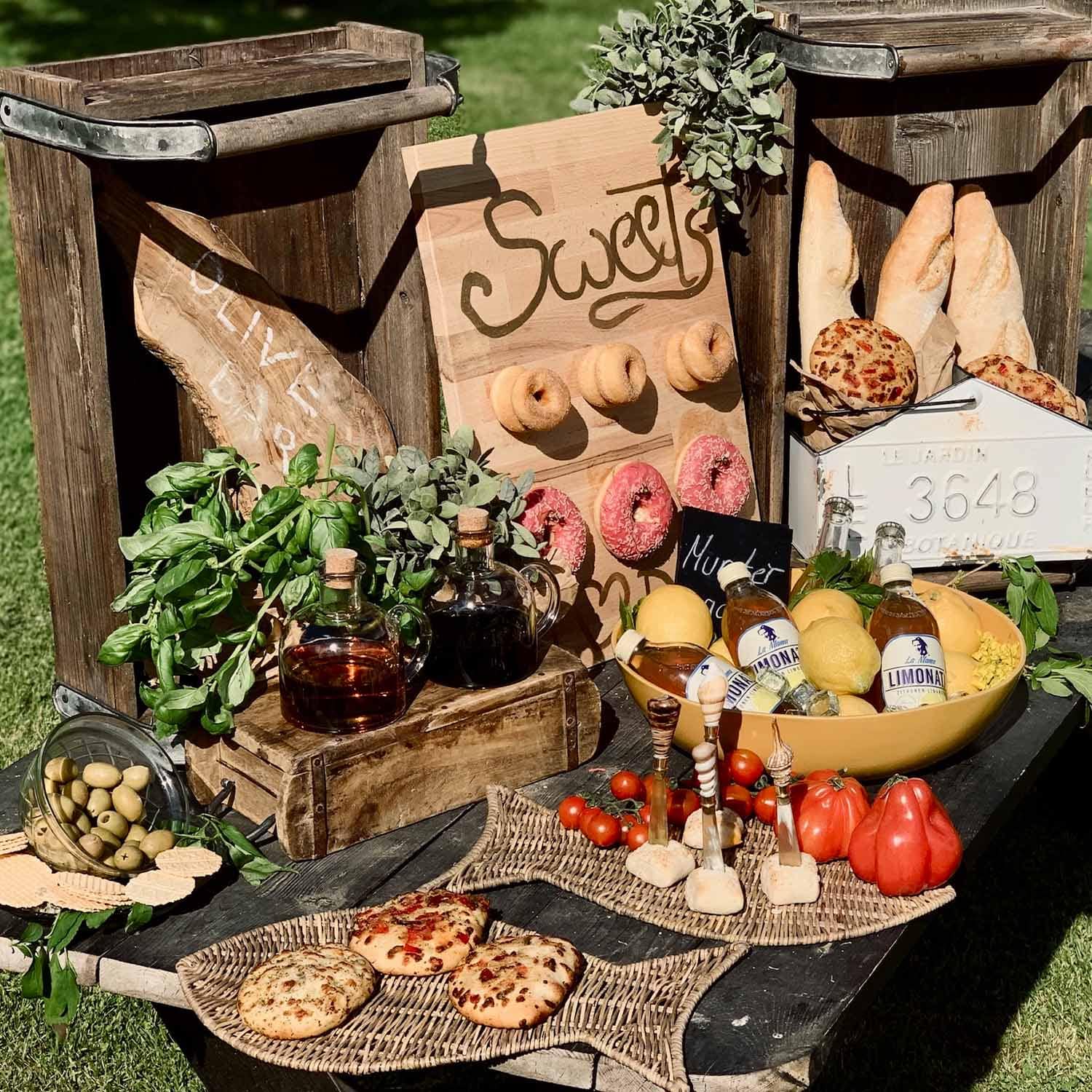 Rustieke tafel met houten kisten, brood, olijven, kruiden en limonade buiten in de zon