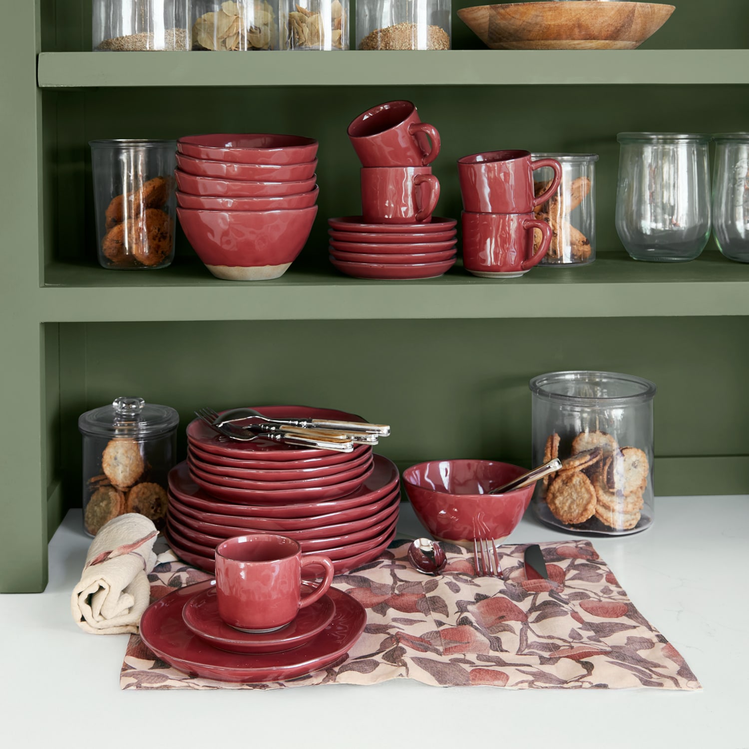 Set rood keramisch servies op groene plank met koekjes in glazen potten