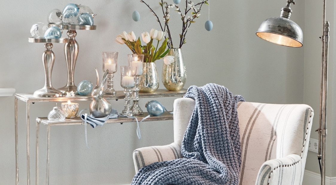 Gezellige witte fauteuil met blauwe gebreide deken en metalen kandelaars en decoraties op de achtergrond