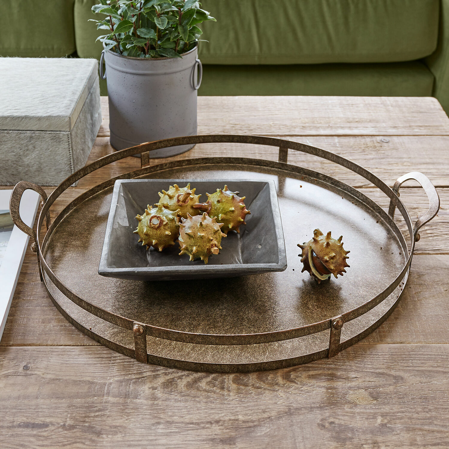 Dienblad Aquivar Ronde metalen dienblad in messingkleur op houten tafel met keramische schaal en decoratieve kastanjes