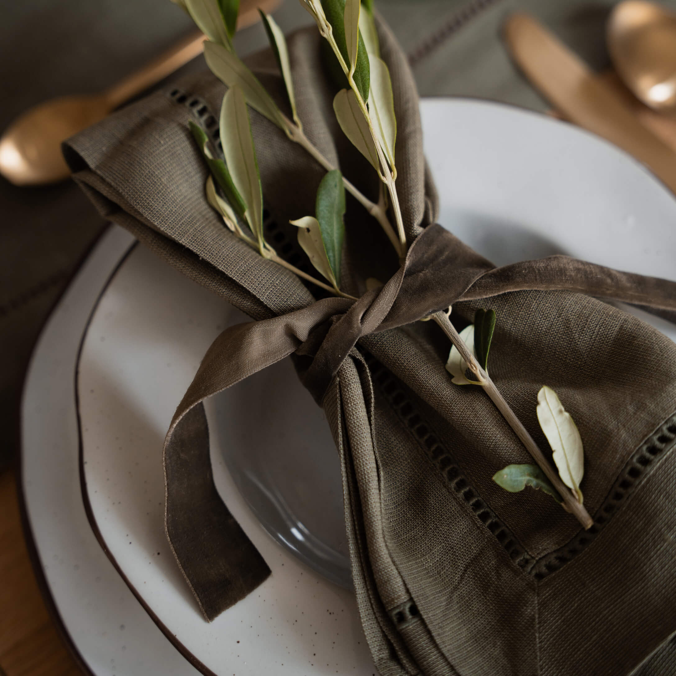 Bruine linnen servet met groene takjes op wit bord voor tafeldecoratie