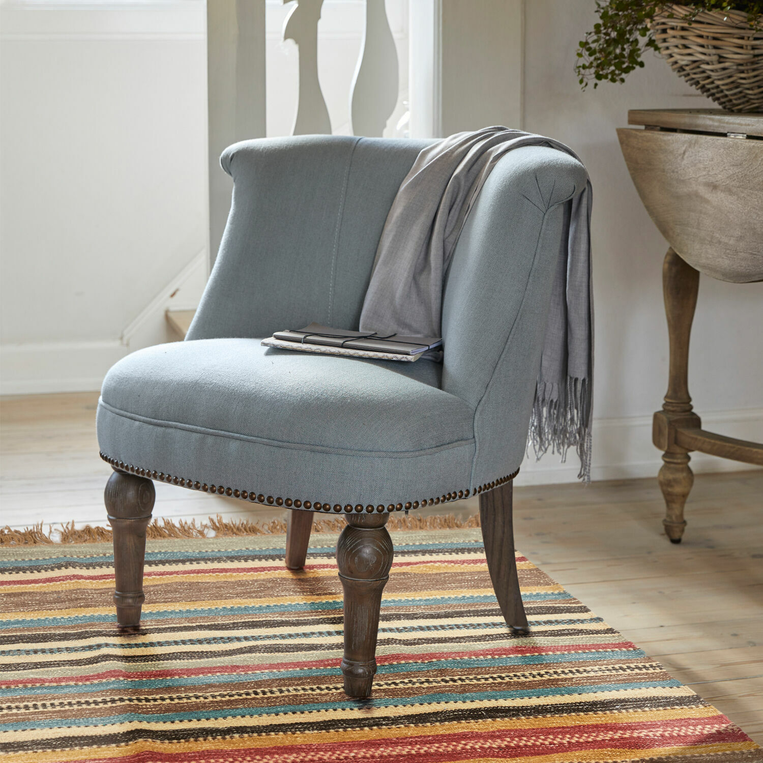 Fauteuil Francet Grijze gestoffeerde stoel met houten poten op kleurrijk vloerkleed in lichte kamer