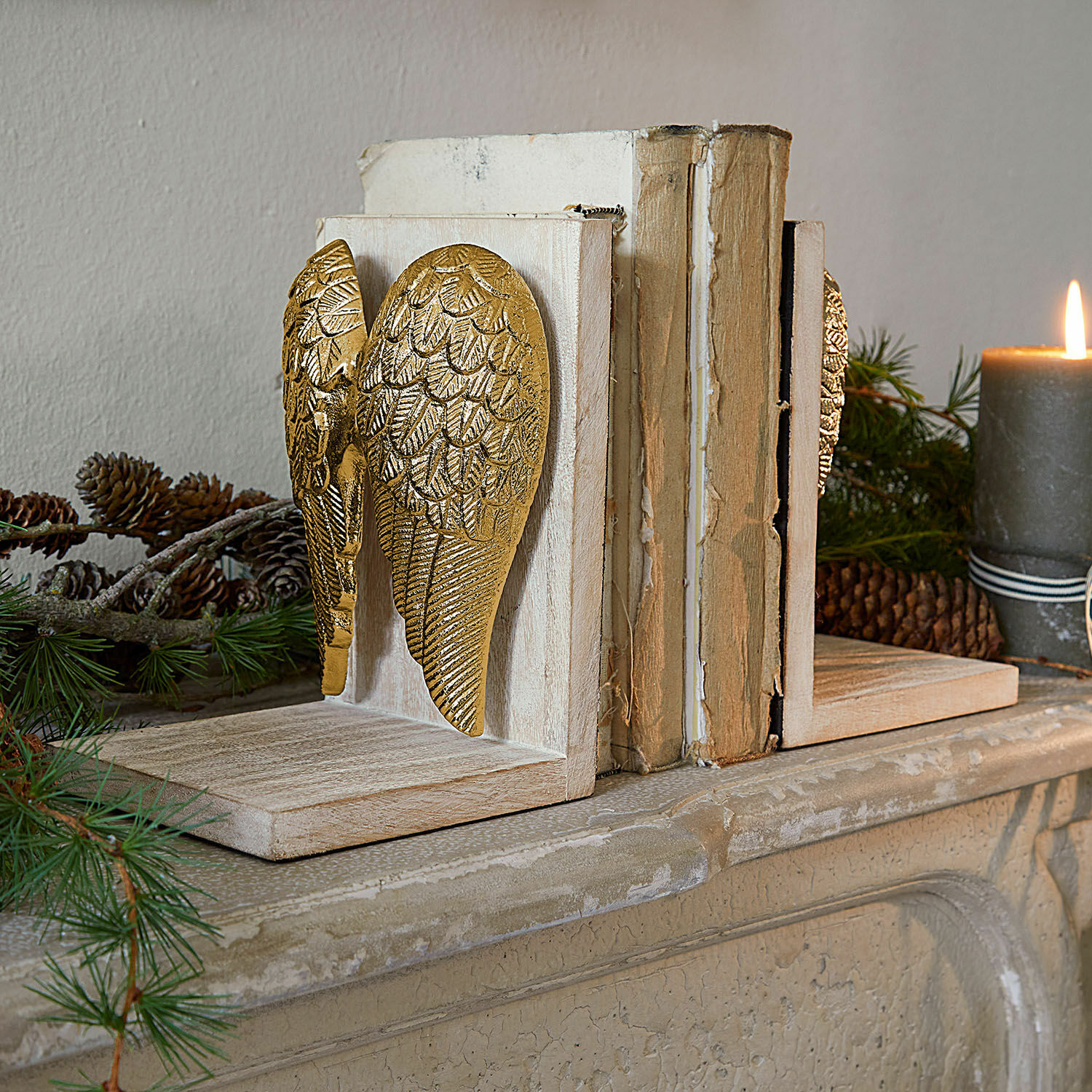 Houten boekensteunen met gouden engelenvleugels, schoorsteendecoratie met dennenappels en kaars