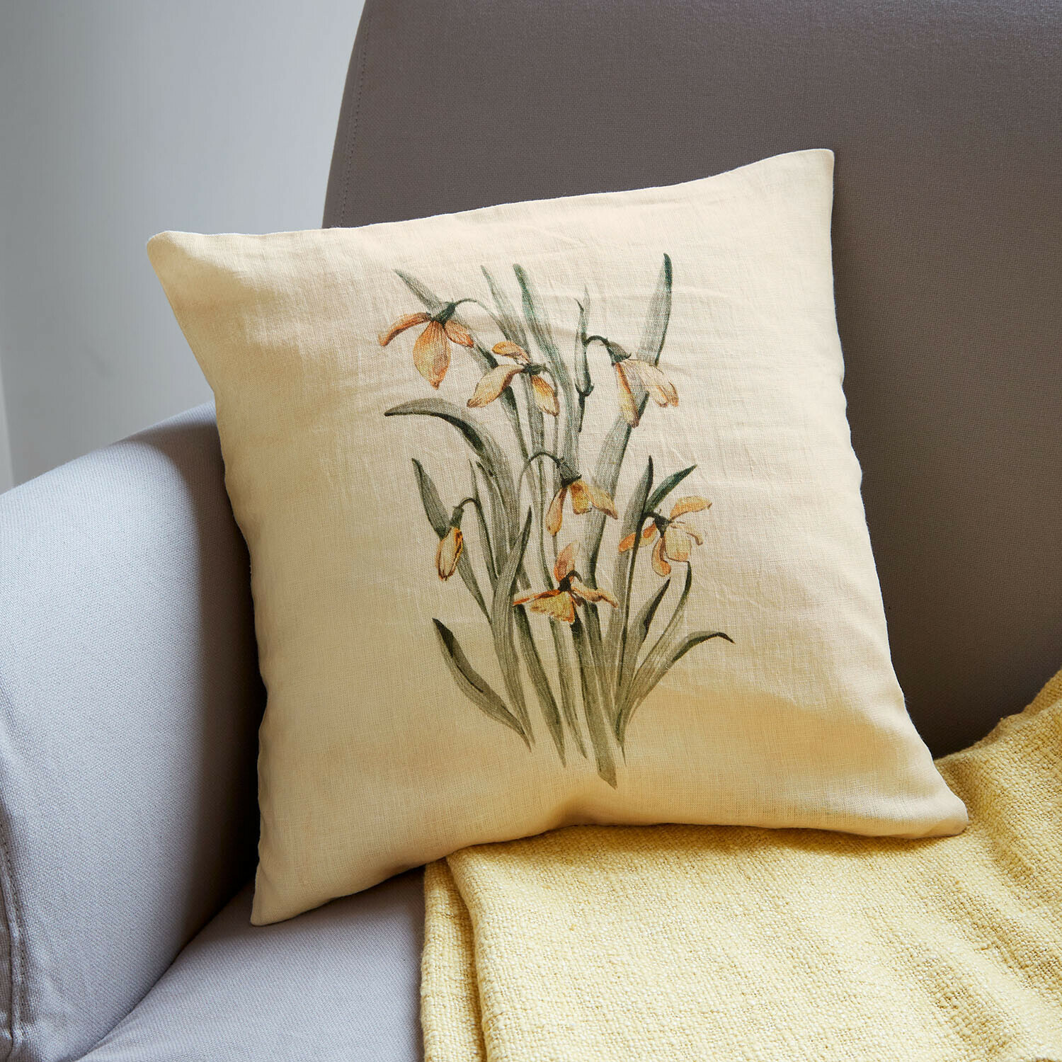 Beige linnen kussen met gele bloemenprint op grijze bank met gele deken