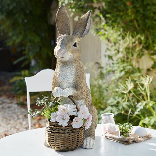 Decoratief konijn van kunststof in natuurlijke kleur met rieten mand en bloemen op tuintafel