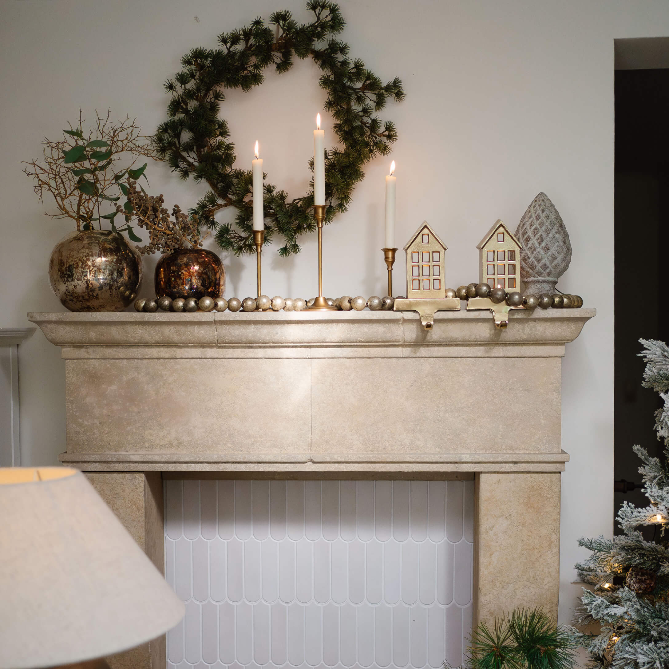 Beige stenen open haard met groene krans, gouden kandelaars en feestelijke kerstdecoraties