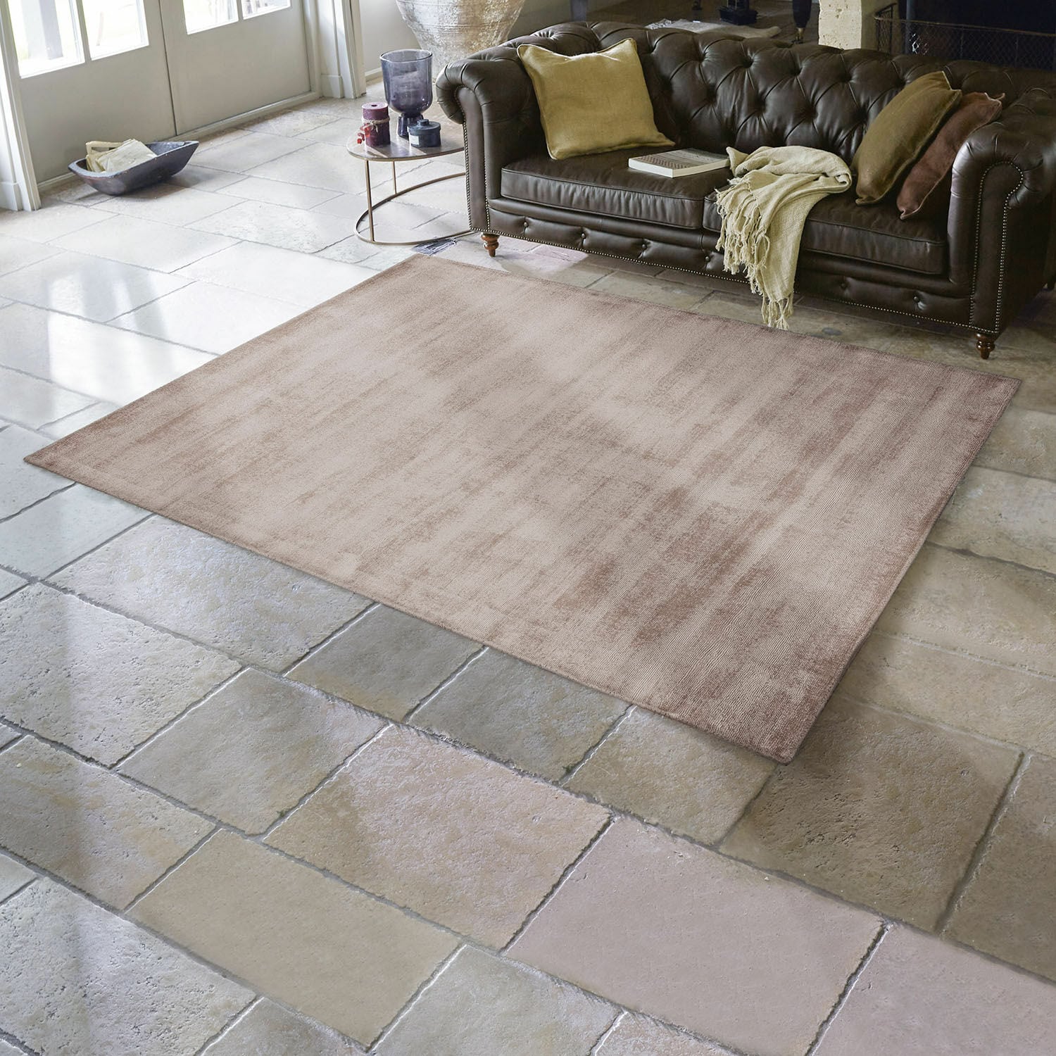Vloerkleed Mariselle Beige vloerkleed van zacht materiaal op stenen vloer in woonkamer met bruine leren bank