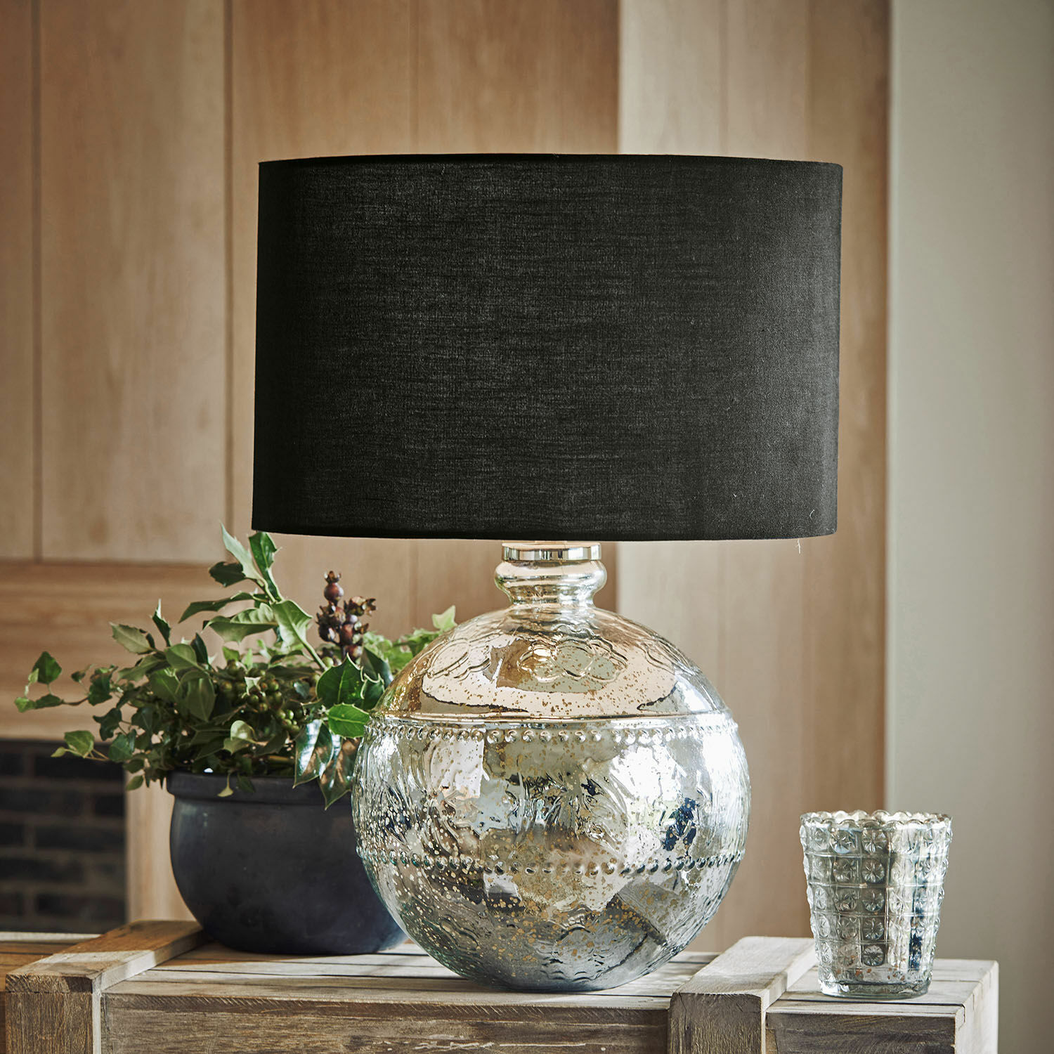 Decoratieve tafellamp met zilverkleurige glazen voet en zwarte kap op houten tafel
