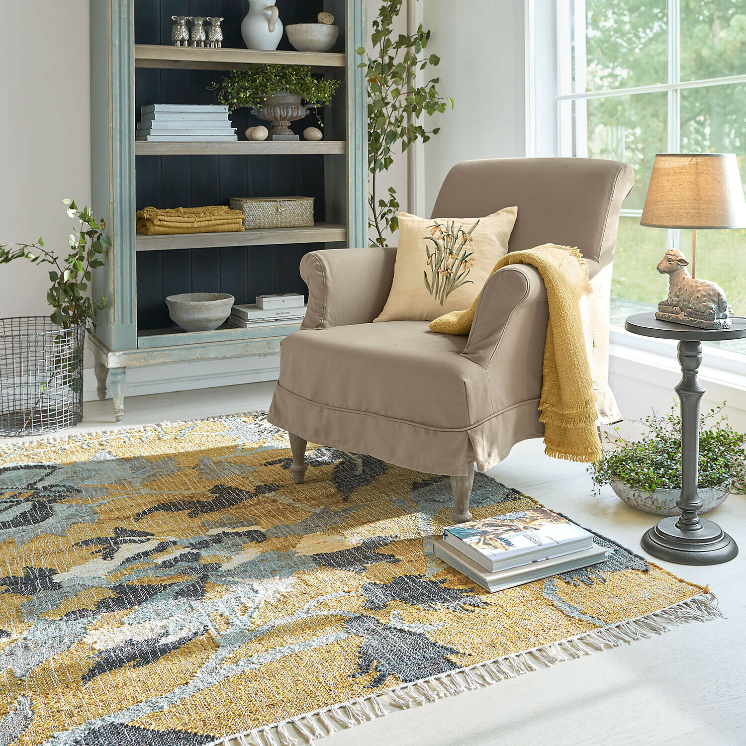 Beige stoffen fauteuil met gele deken en kussen op kleurrijk vloerkleed in lichte woonkamer