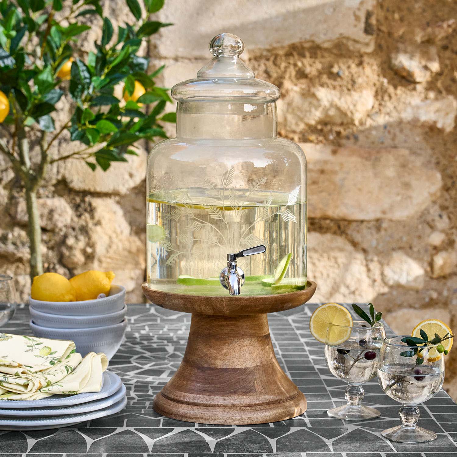 Glazen drankdispenser met deksel op houten standaard gevuld met water en citroenschijfjes