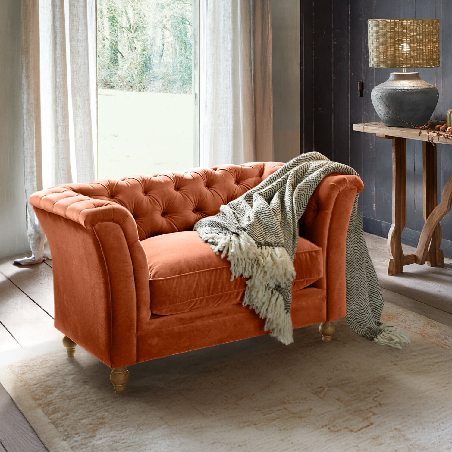 Oranje fluwelen Chesterfield-bank met grijze deken in gezellige woonkamer met lamp en houten tafel