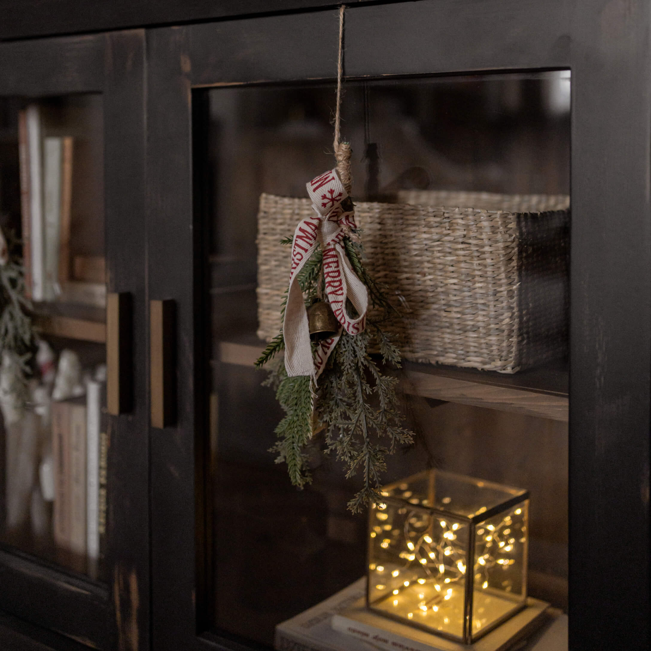 Kerstdecoratie met groene takken, bel en lint aan zwarte kast met mand en LED-licht
