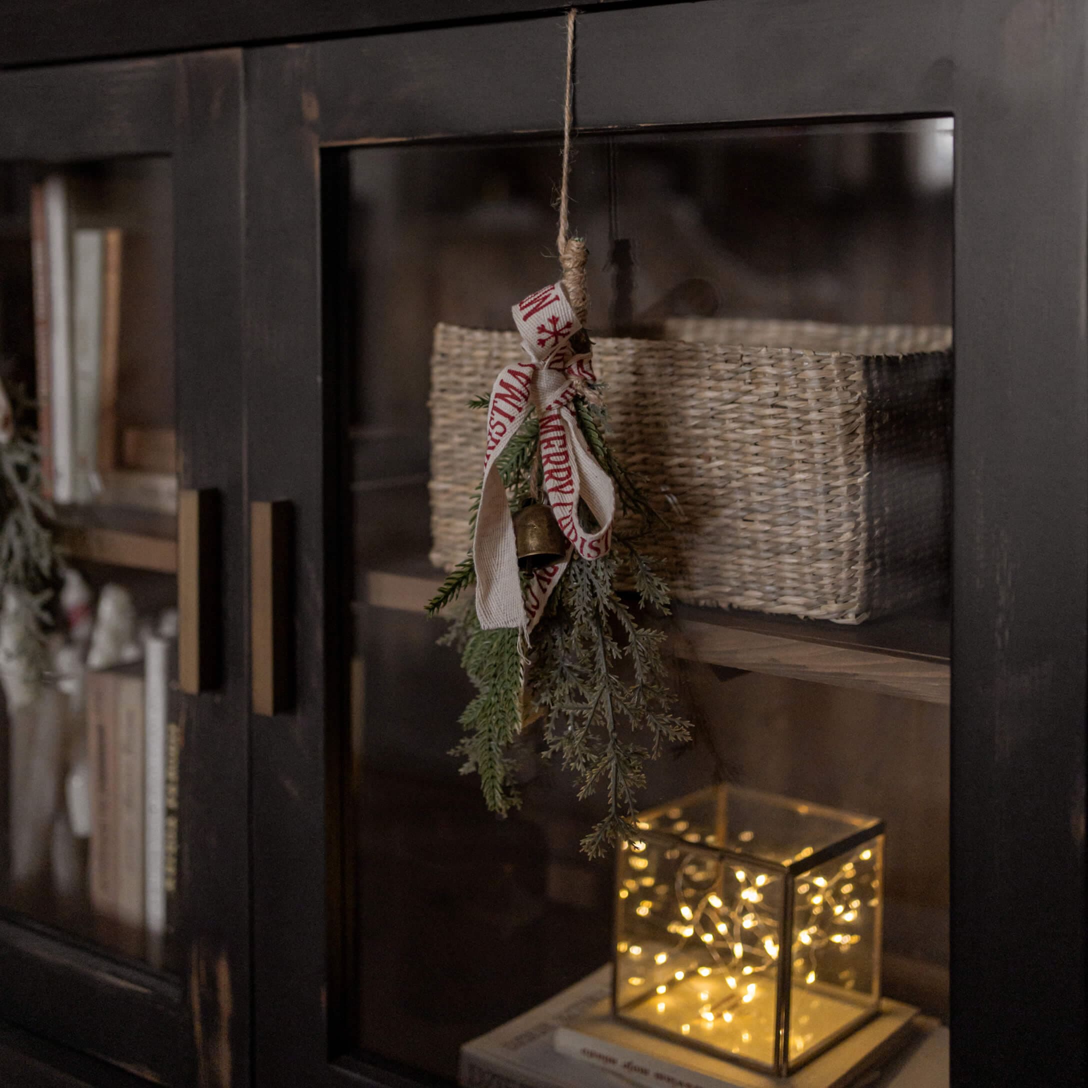 Kerstdecoratie met groene takken, bel en lint aan zwarte kast met mand en LED-licht