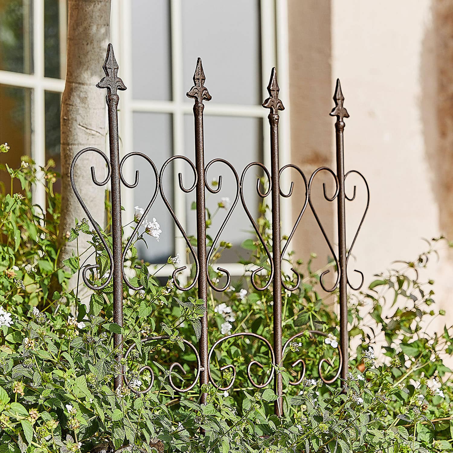 Trellis Nectarise Decoratief metalen tuinhek in roestbruin met hartmotief, omgeven door groene planten en witte bloemen