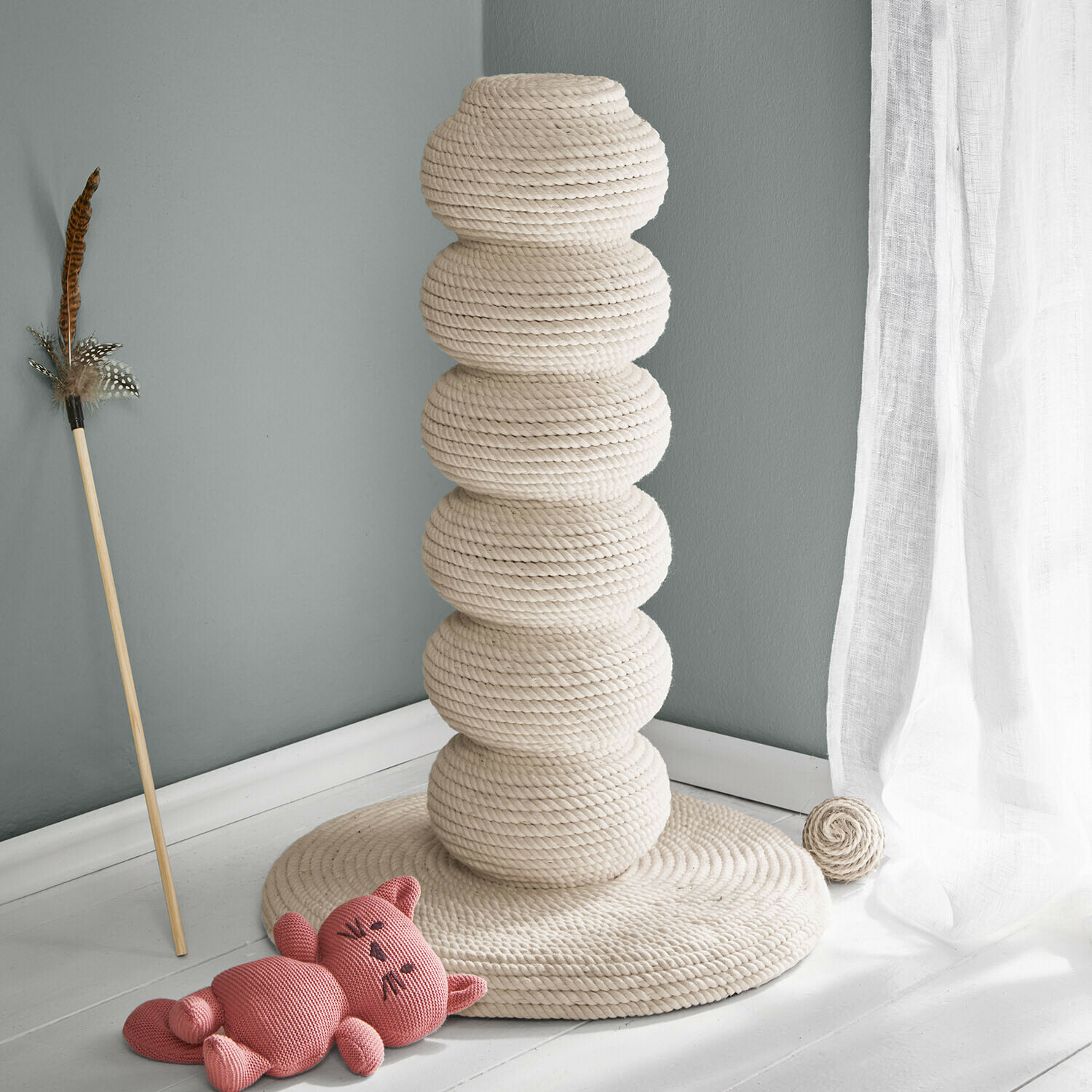 Kattentoren van natuurlijke crèmekleurige touw met speelgoed en roze pluchen kat op de vloer