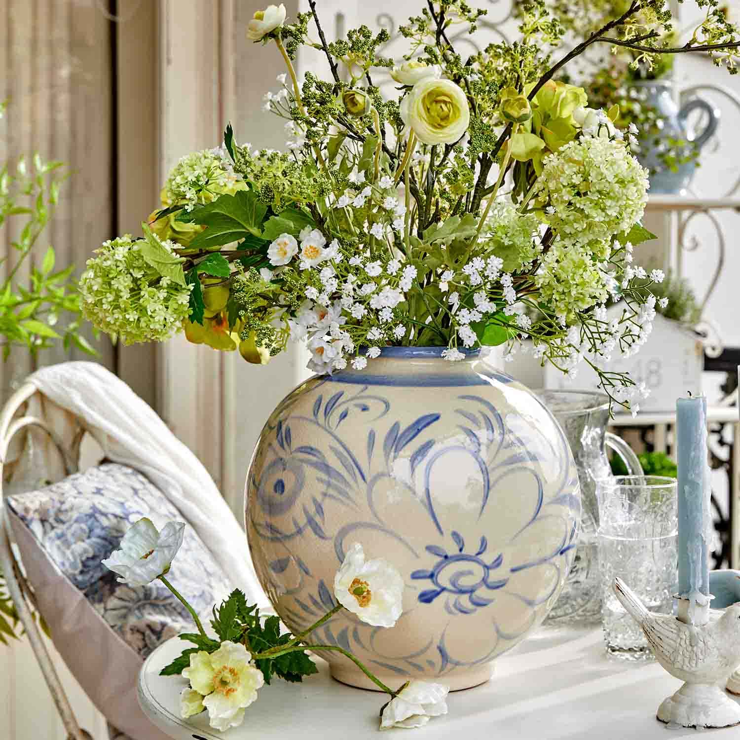Ronde keramische vaas met blauw bloemmotief en boeket groen-witte bloemen op tafel