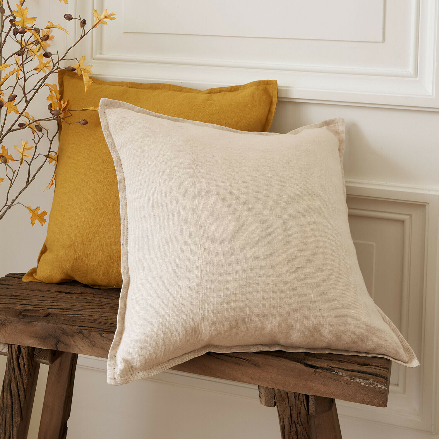 Kussenhoes set van 2 Orsavine Twee decoratieve linnen kussens in beige en mosterdkleur op een rustieke houten bank