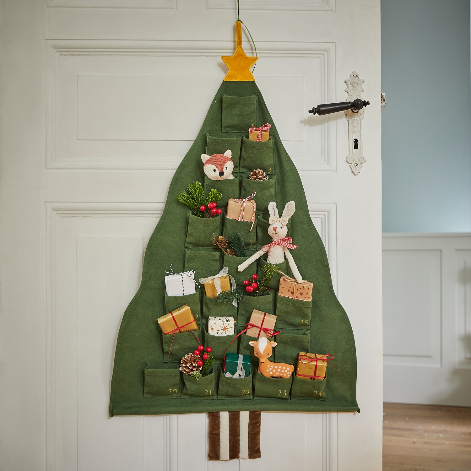 Groene stoffen adventskalender in de vorm van een kerstboom met zakjes en kerstdecoraties