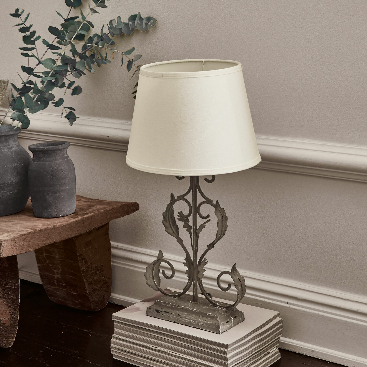 Tafellamp met grijze metalen voet en crèmekleurige kap op houten vloer