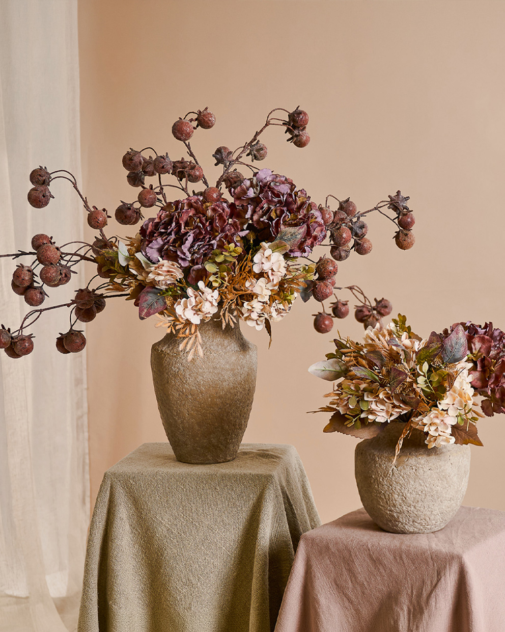 Twee decoratieve beige stenen vazen met herfstbloemen en gedroogd fruit op gedekte tafels