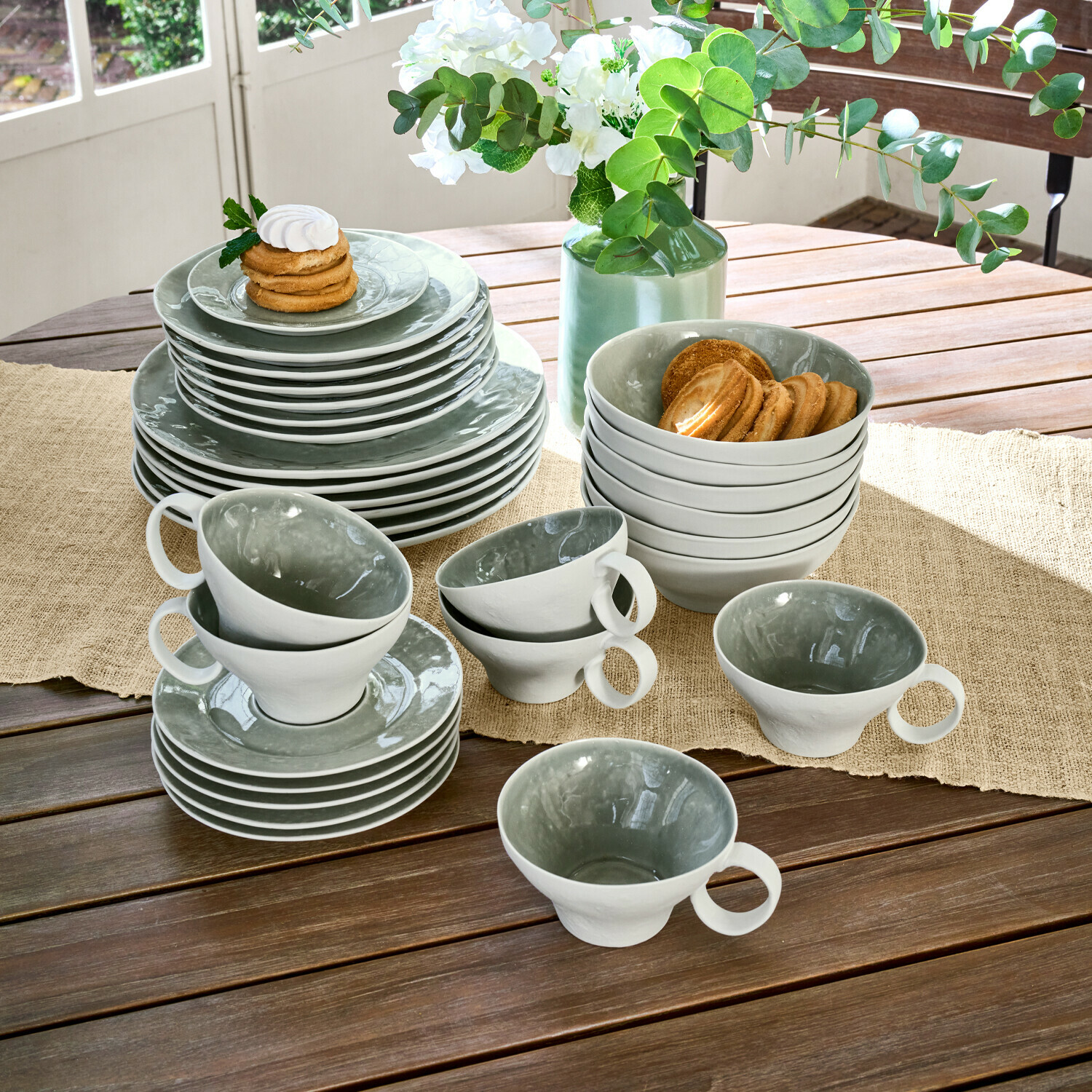Grijs-witte keramische servies set op houten tafel met koekjes en bloemstuk