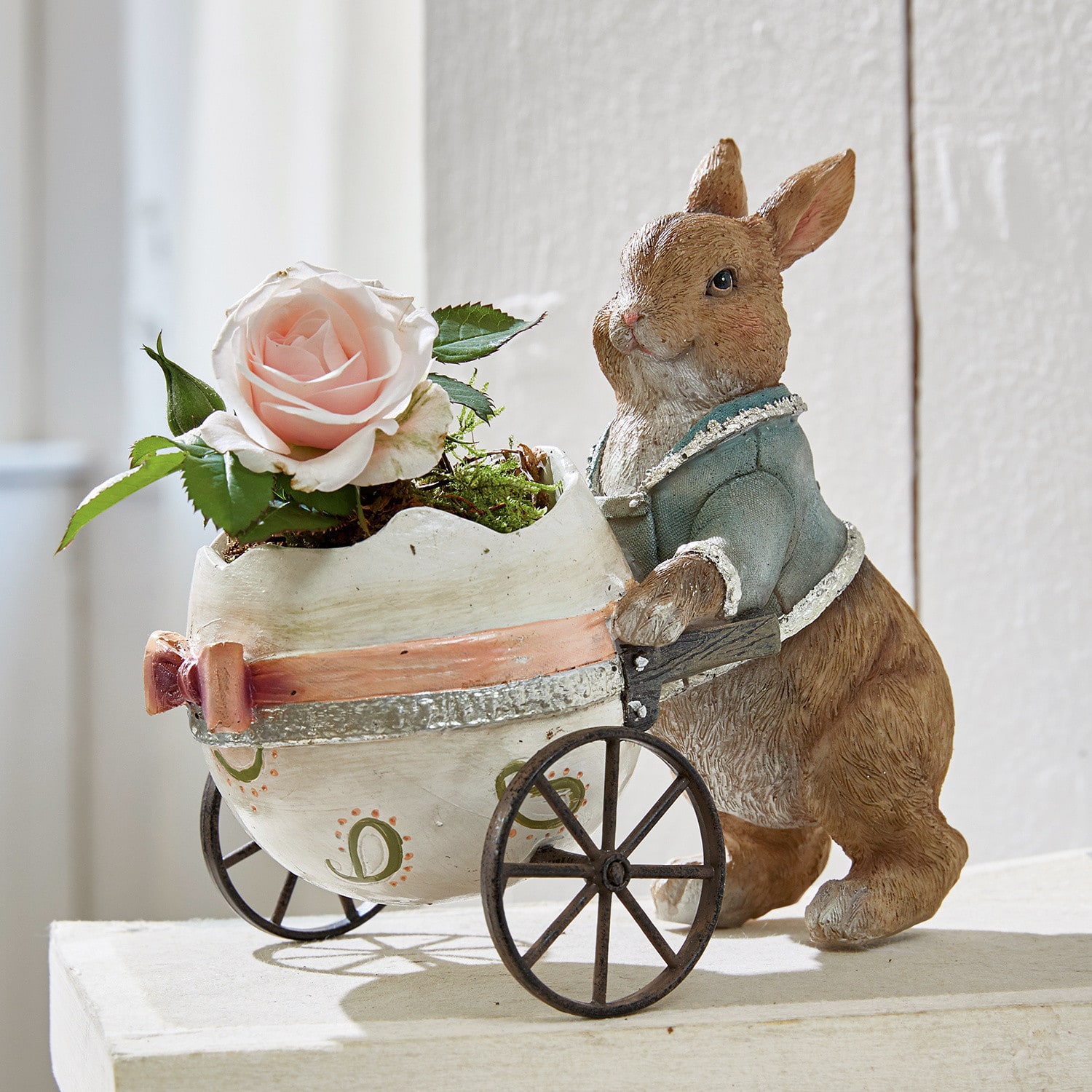 Bruine konijnenfiguur van materiaal duwt witte kar in eivorm met roze roos