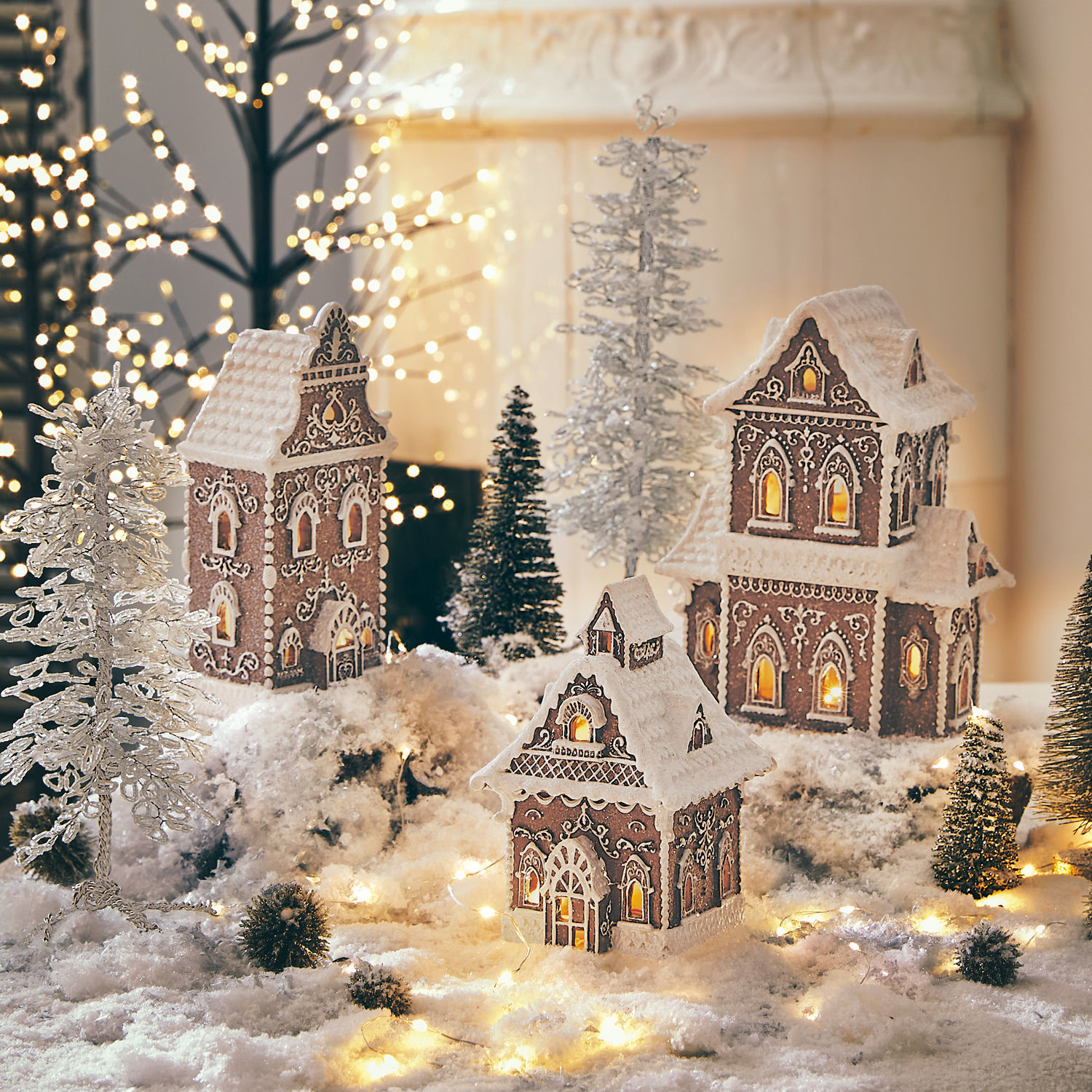 Decoratiehuisje set van 3 Anyama Decoratieve peperkoekhuisjes met witte glazuur en lichtjes op een besneeuwde achtergrond met dennenbomen