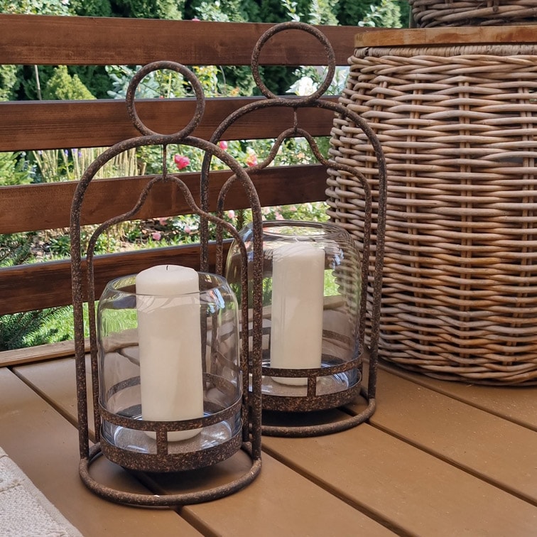 Twee decoratieve lantaarns met metalen frame en witte kaarsen op een houten tafel in de tuin