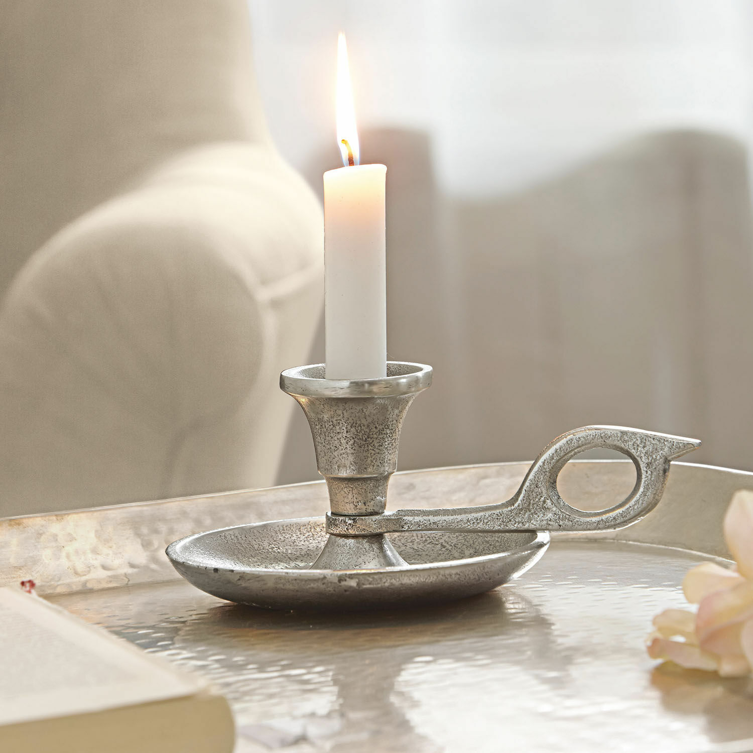 Zilverkleurige metalen kandelaar met witte brandende kaars op decoratieve tafel