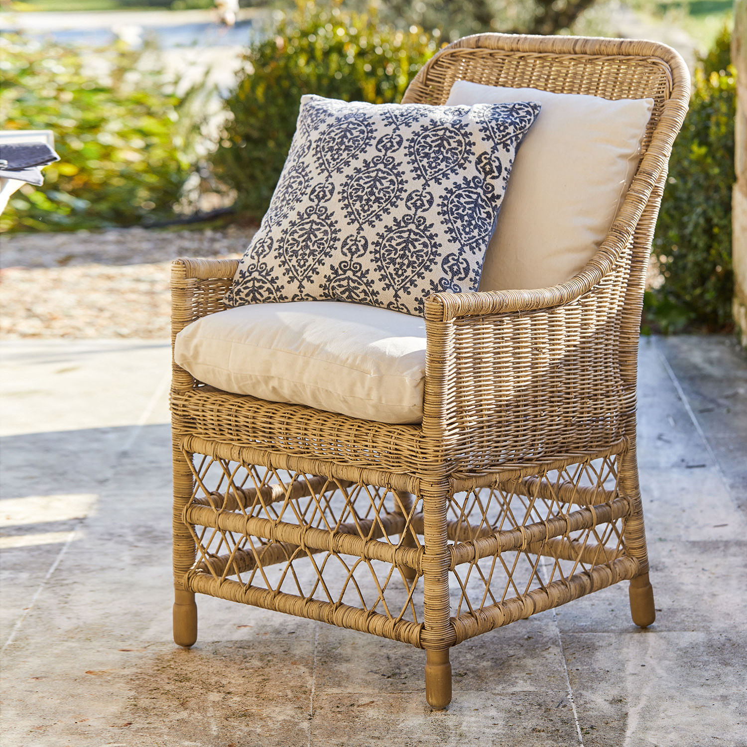 Fauteuil Giepmare Rotan stoel met crèmekleurige kussens en blauw patroon sierkussen, stijlvolle tuinmeubelen