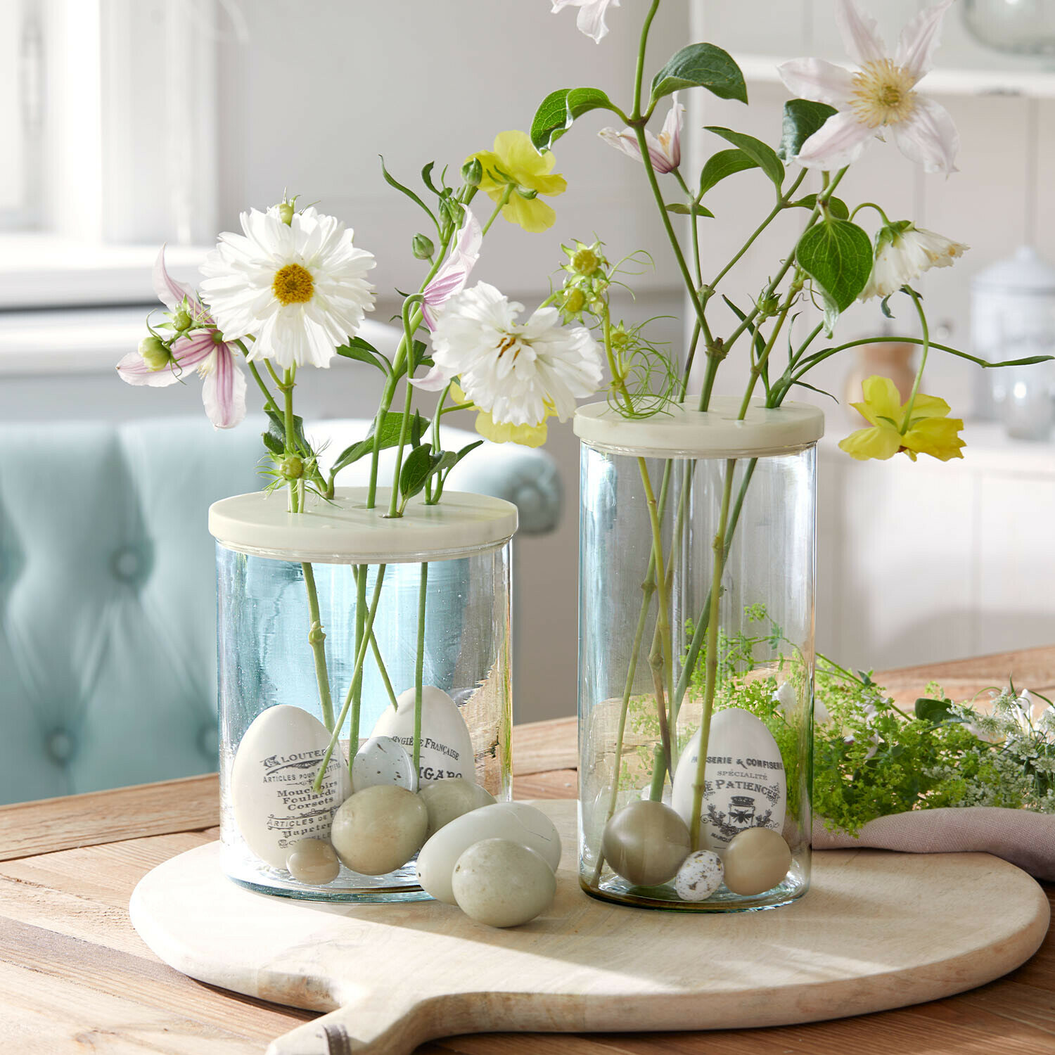 Glazen vazen met witte en groene decoratieve eieren en bloemen op een houten snijplank