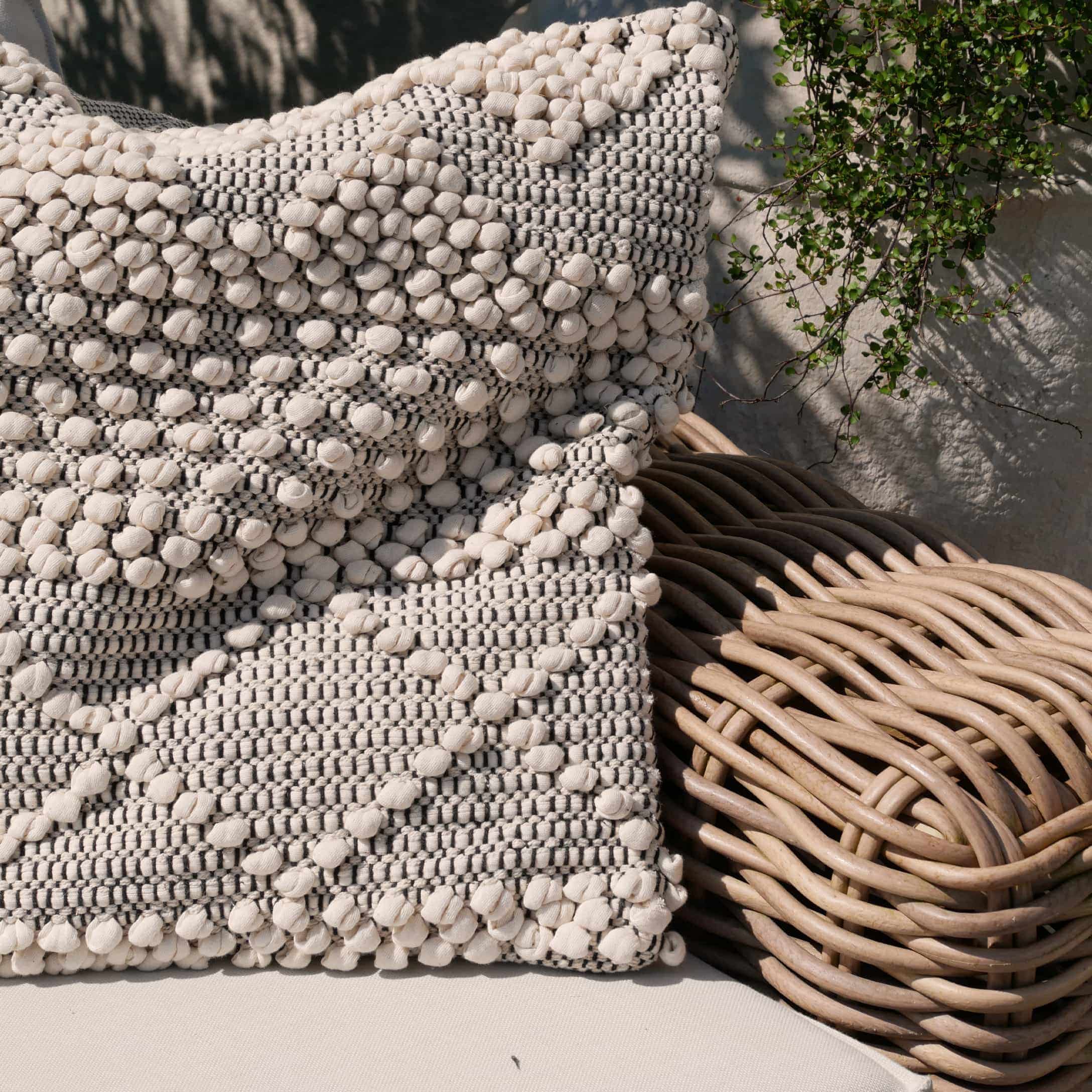 Decoratief katoenen kussen in crème-grijs op een rotan stoel, boho stijl
