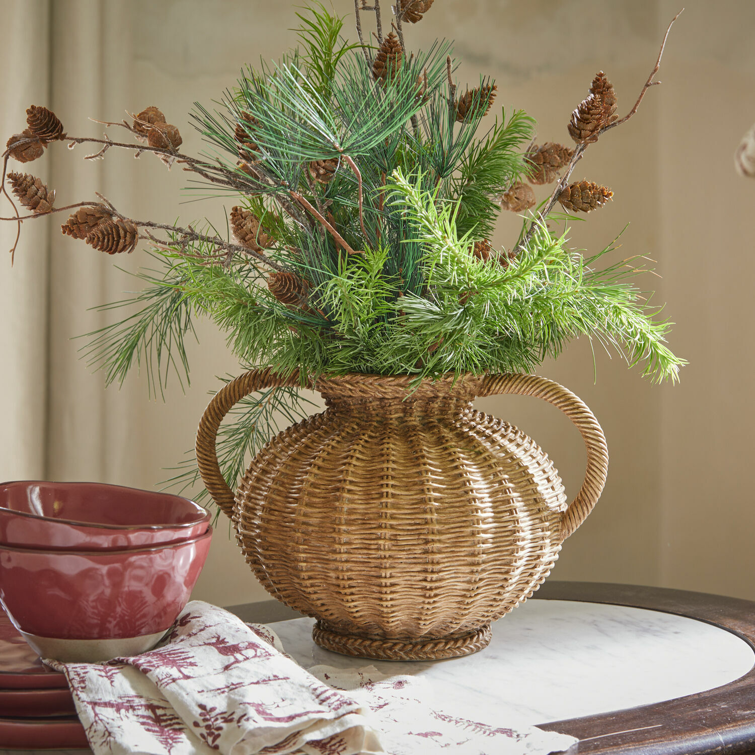 Vaas Kaelvik Decoratieve rieten vaas met handvatten, groene takken en dennenappels op tafel met rood keramiek