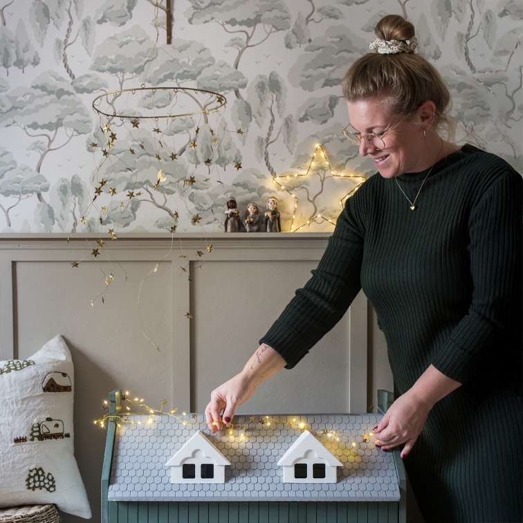 Vrouw versiert grijze houten kist met stervormige LED-lichtjes in een gezellige kamer