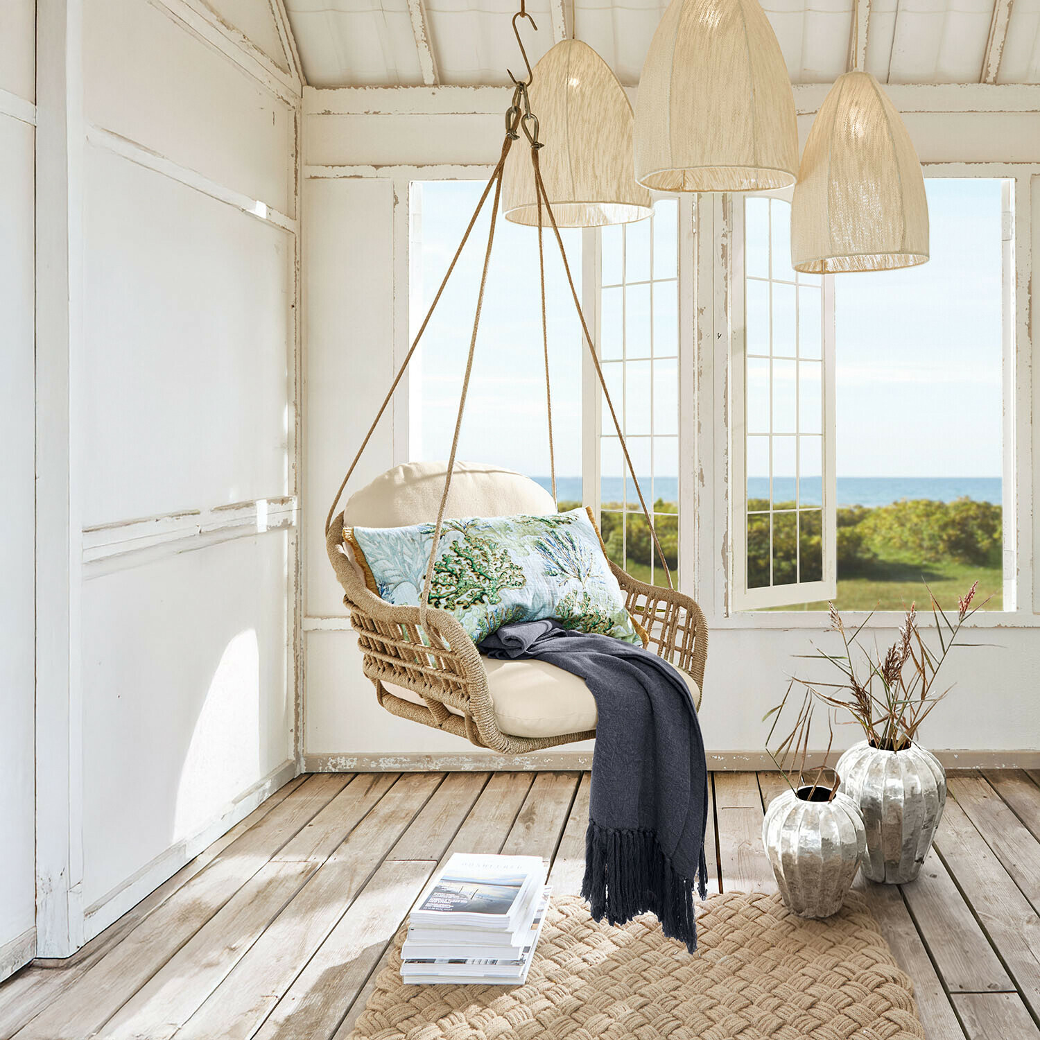 Hangstoel van gevlochten touw met crème kussen en decoratief kussen met zee-thema in lichte kamer