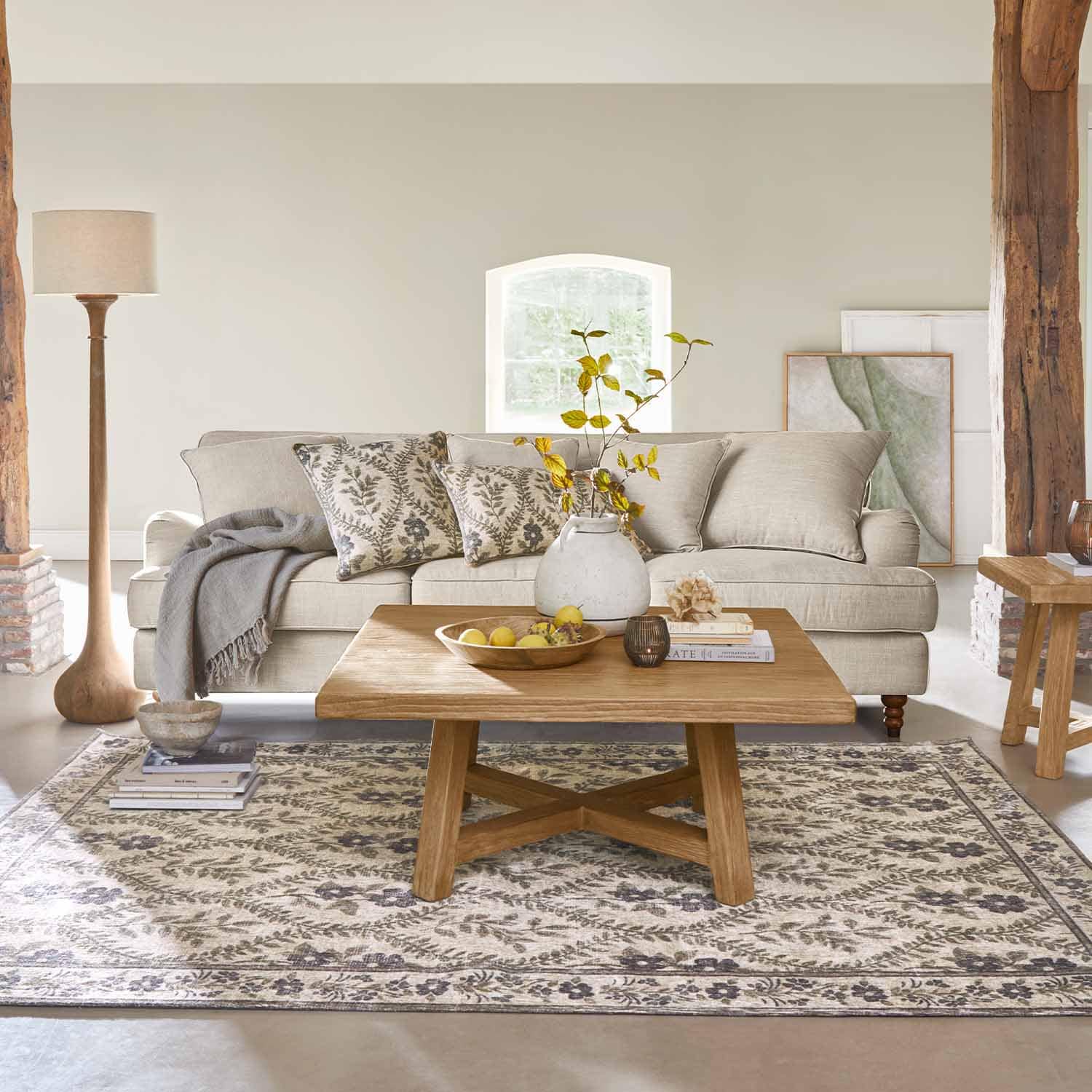 Beige stoffen bank met decoratieve kussens en houten salontafel op een patroon vloerkleed
