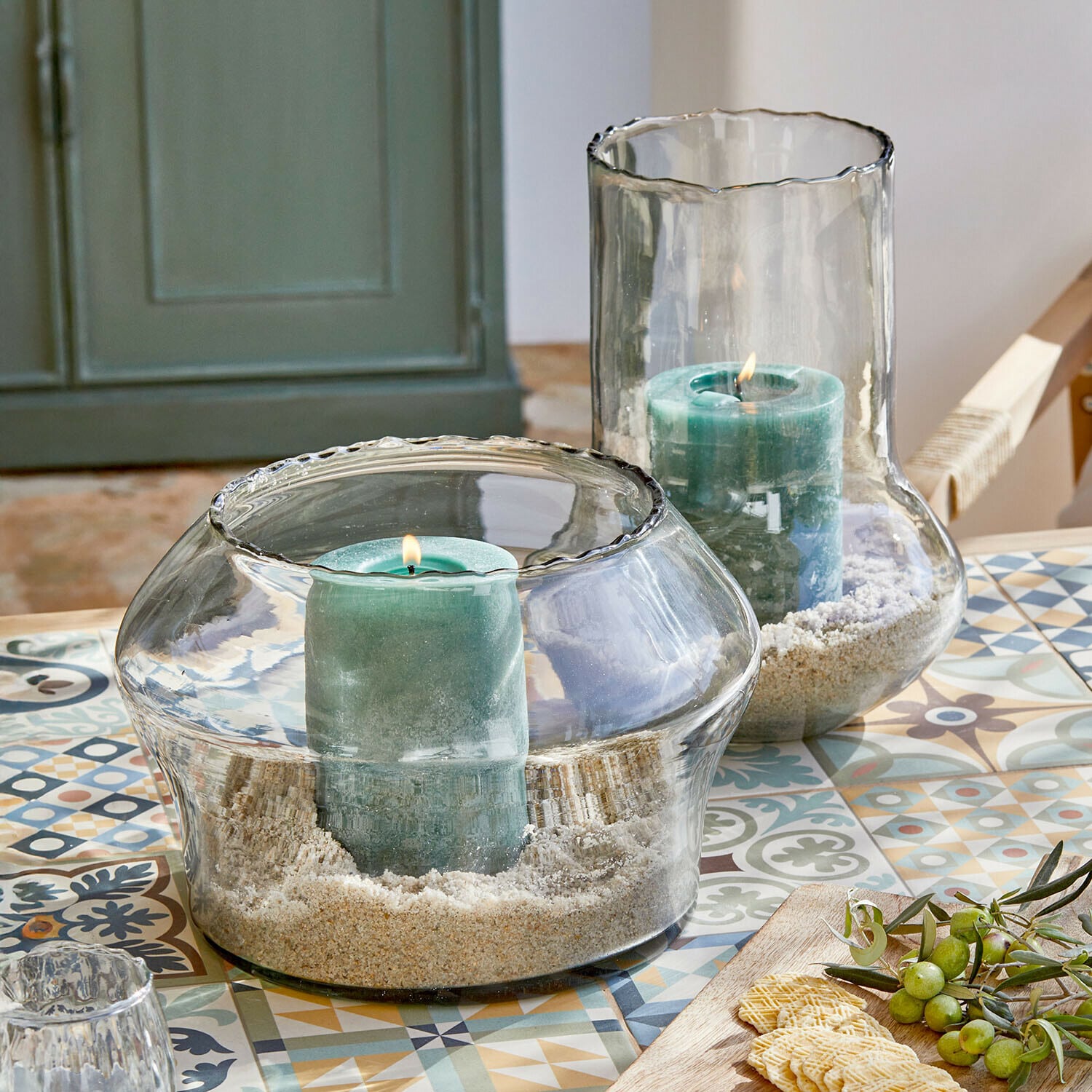 Windlicht set van 2 Lumiras Glazen windlichten met groene kaarsen en zand op een kleurrijke tafel met decoratieve patronen