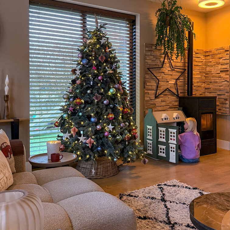 Gezellige woonkamer met versierde kerstboom, zachte bank en kind dat met poppenhuis speelt