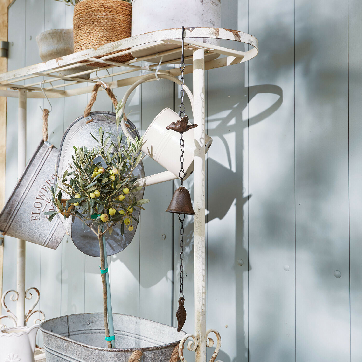 Metalen tuindecoratie met bel en vogel, witte gieter en plant in metalen pot