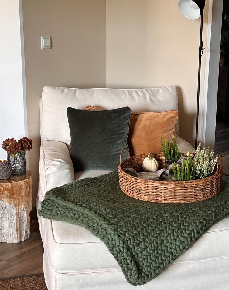 Beige fauteuil met groene en oranje kussens, gevlochten mand met decoraties op groene deken