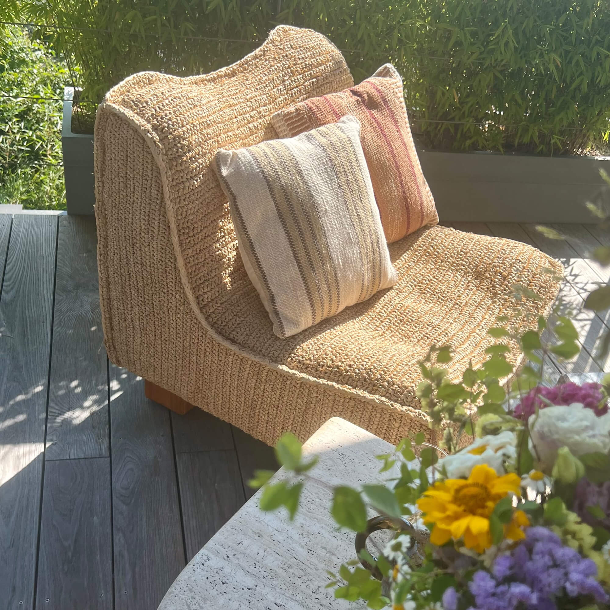 Beige stoel van gevlochten materiaal met twee decoratieve kussens op een bloementerras