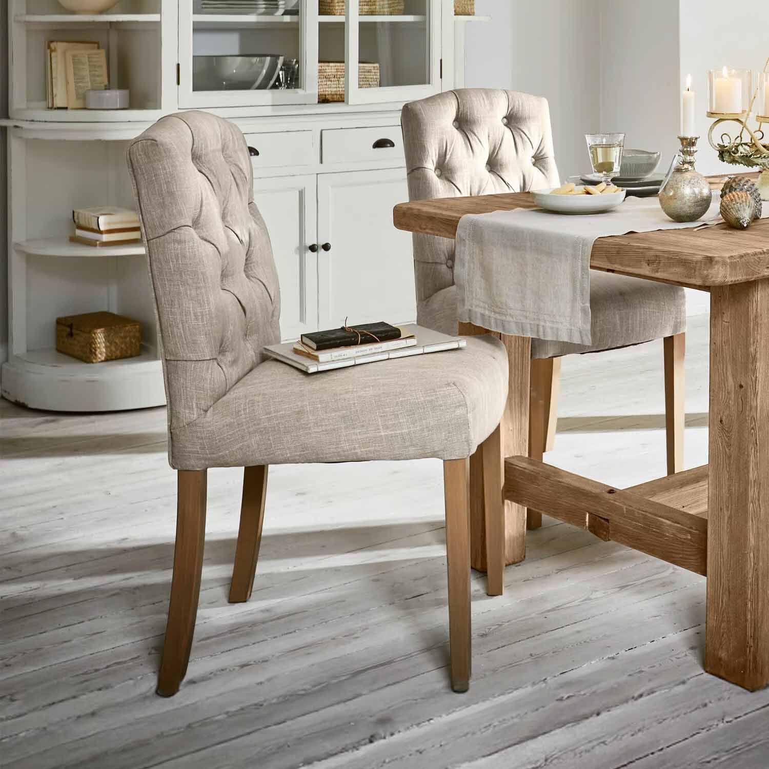 Beige gestoffeerde stoel met houten poten bij houten tafel in lichte eetkamer