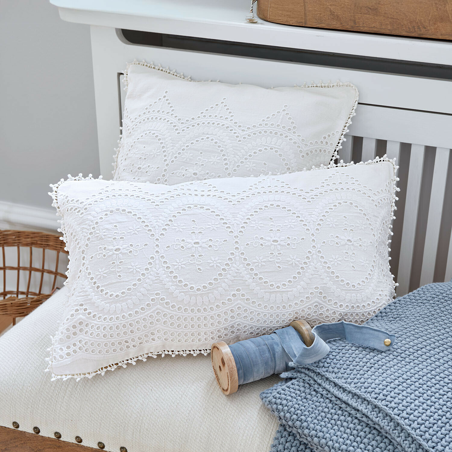 Witte katoenen kussens met borduurwerk en opengewerkt patroon op bank met blauwe gebreide deken