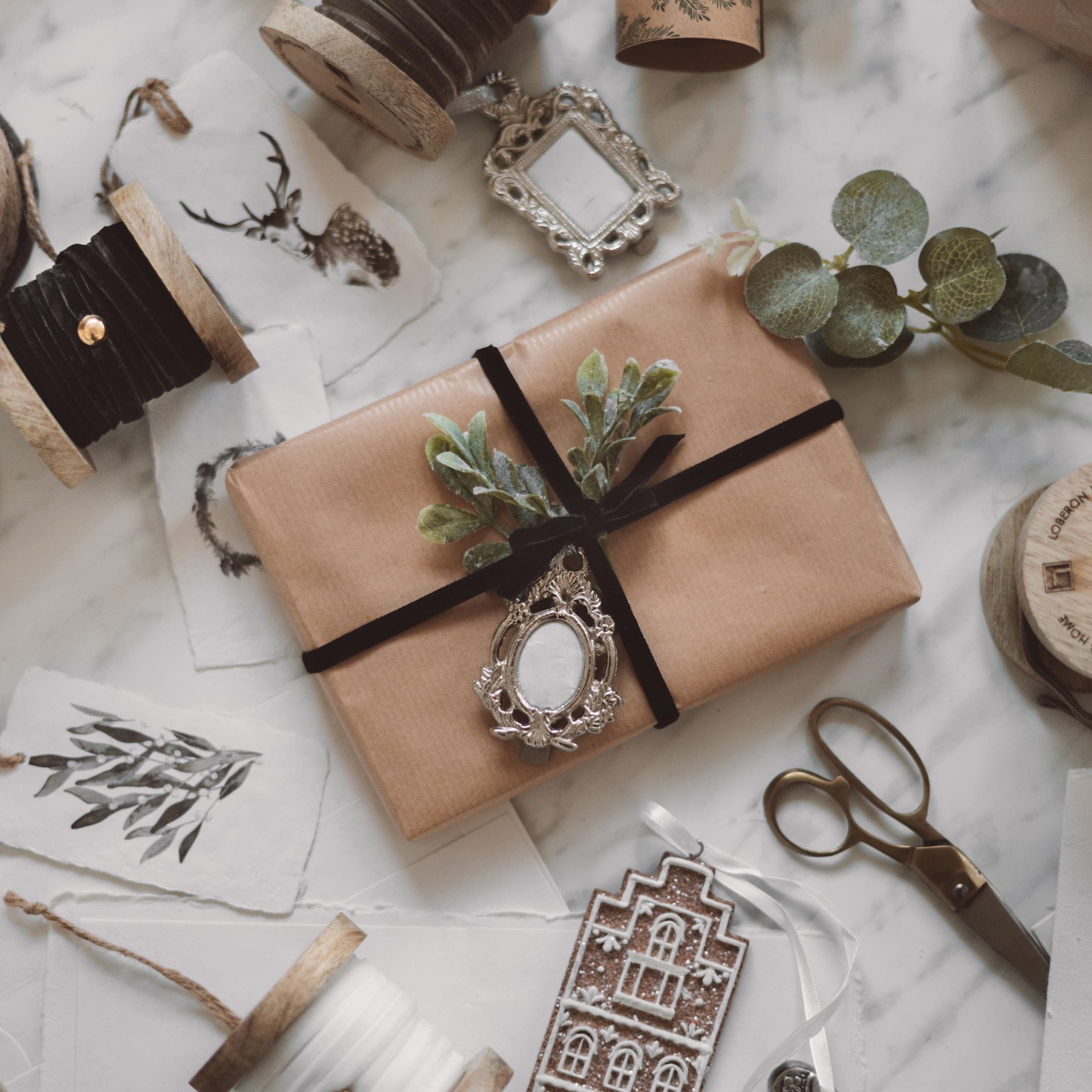 Cadeau verpakt in bruin papier met zwart lint en groene bladeren op marmeren achtergrond met decoraties