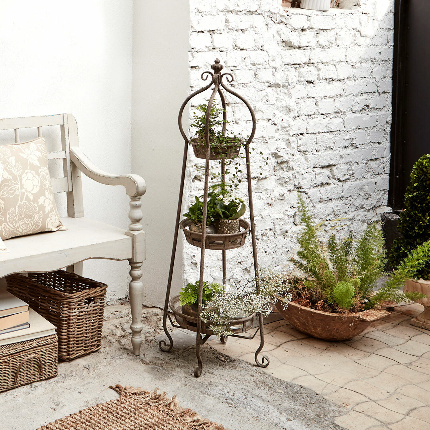 Rustieke metalen plantenstandaard met drie niveaus, beplant, in lichte ruimte met witte bank